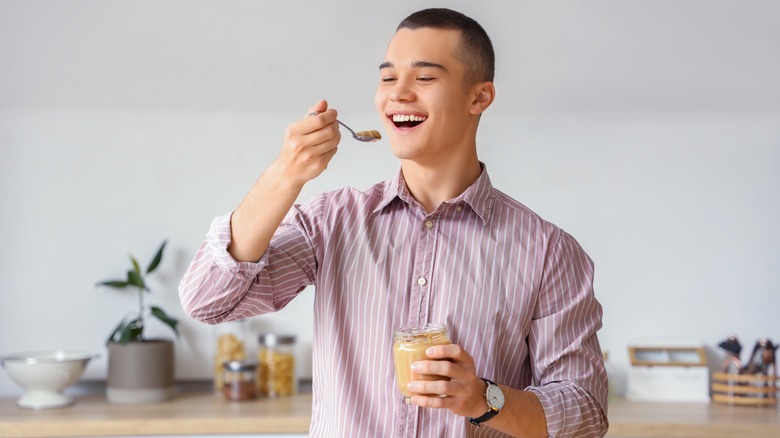 young man eating peanut butter from a jar