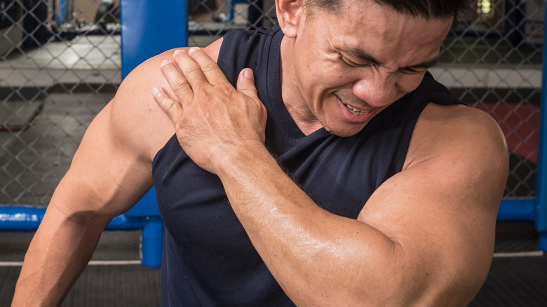 a man in the gym holds his shoulder in pain