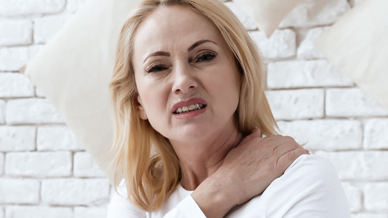 a woman in bed holds her shoulder wincing
