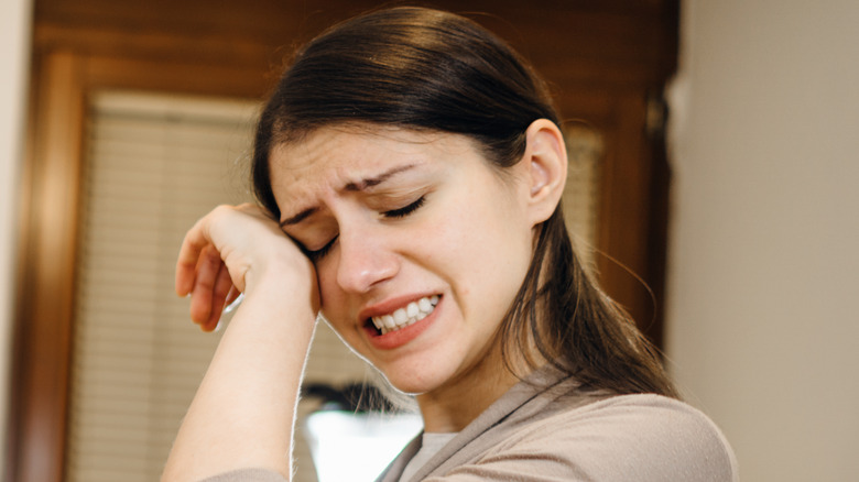 Woman rubbing eye while cooking in kitchen