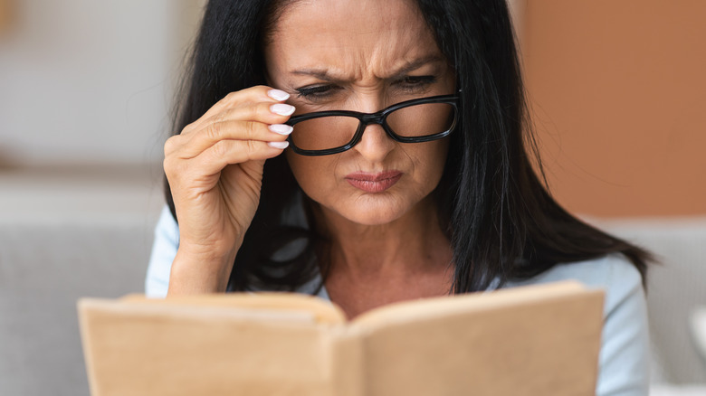 Woman holding glasses squinting while reading