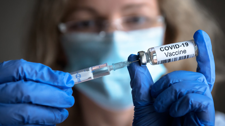 female professional holding up a COVID-19 vaccine vial and syringe with gloved hands