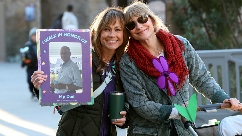 women standing next to a woman holding a sign honoring her father for Alzheimer's Awareness month
