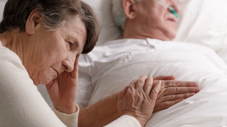Older woman holding the hand of a sick man in bed