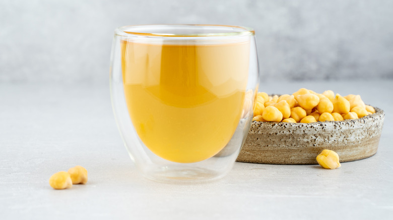 A glass of aquafaba next to a bowl of chickpeas