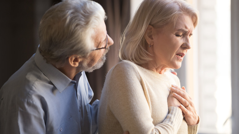 Elderly woman holding hand to her chest, worried partner supporting her