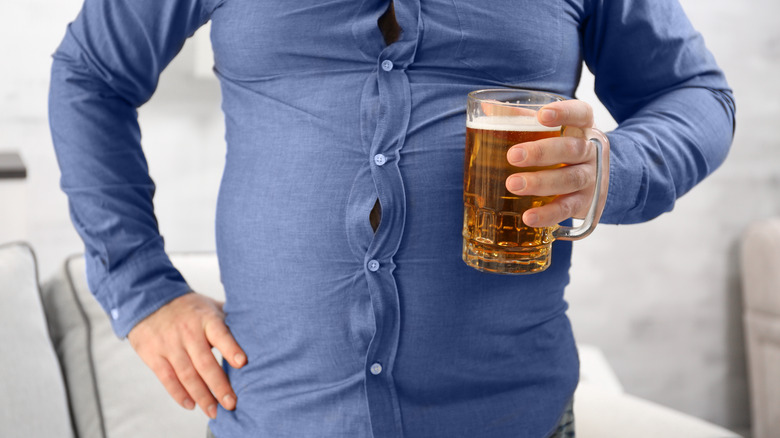 Man holding glass of beer with beer belly wearing shirt with buttons popping out