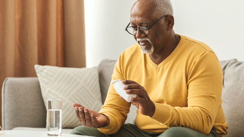 older man sitting on sofa taking viitamins with water