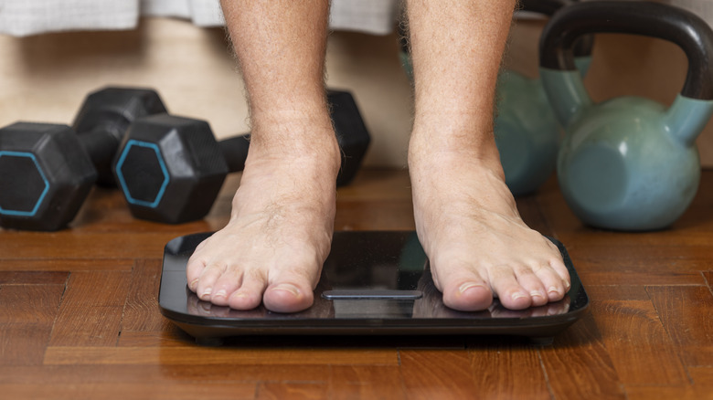 Man standing on scale barefoot surrounded by weights