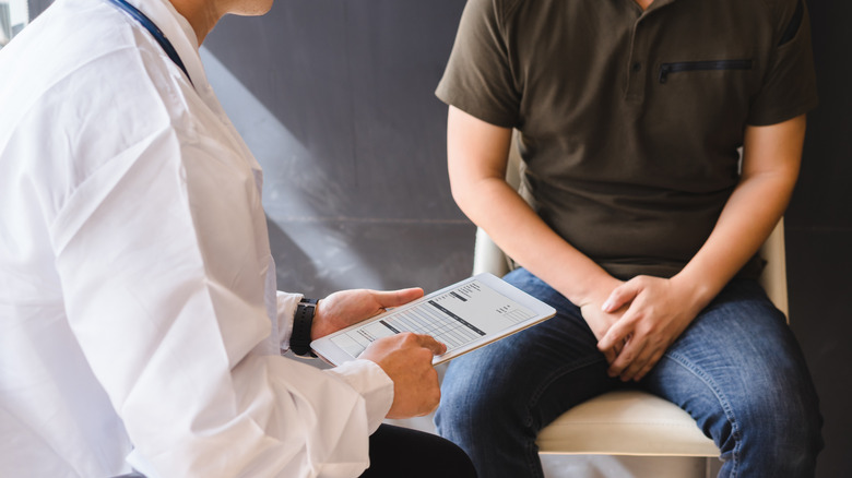 Man holding his crotch while sitting in chair talking with a doctor