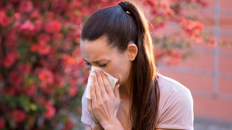 A woman sneezing while outside near flowers