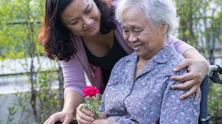 A smiling woman with her arm over a seated senior woman's shoulder