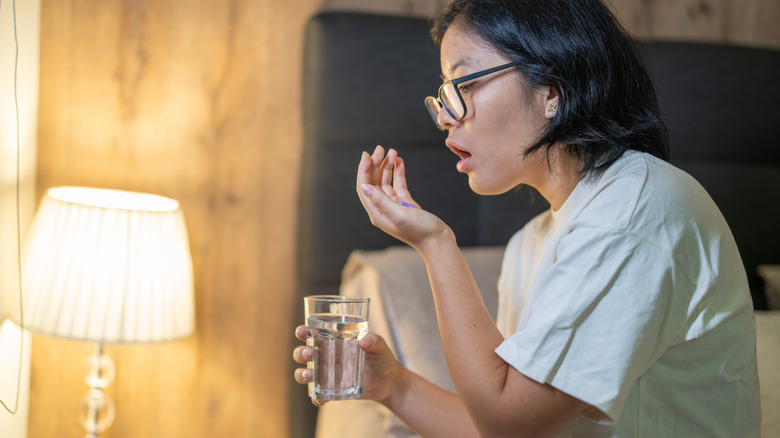 young woman taking vitamin while in bed
