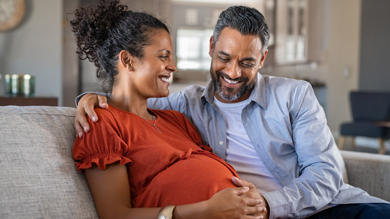 pregnant couple sitting on couch smiling