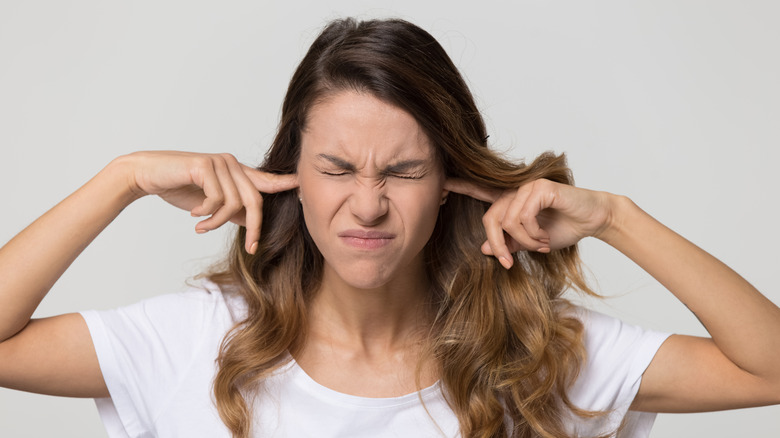 woman plugging her ears with her fingers, looking annoyed by a sound 