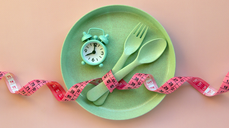 a plate with a clock, fork, spoon and tape measure