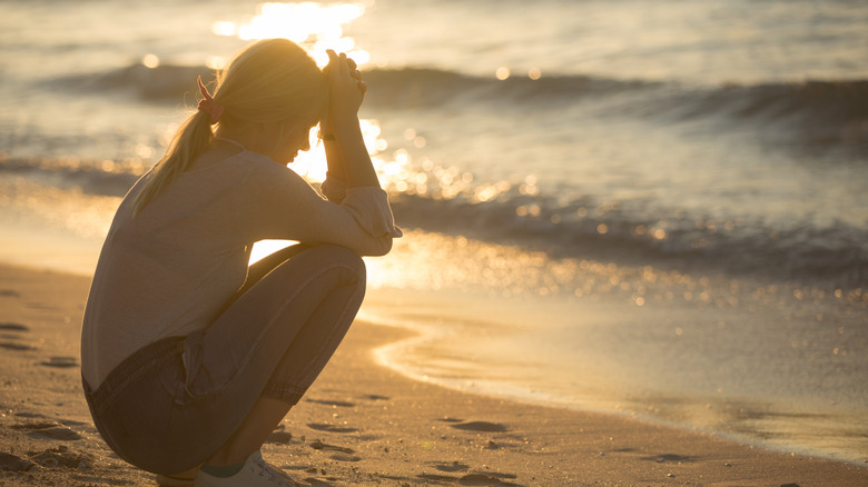 sad woman sitting at edge of ocean