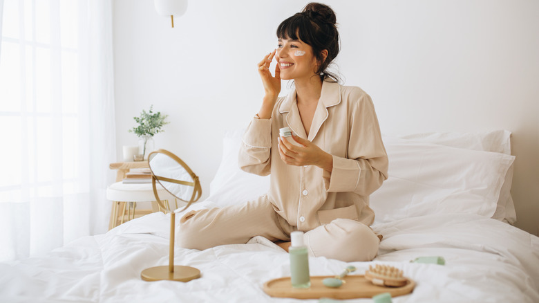 woman applies skincare products in bed