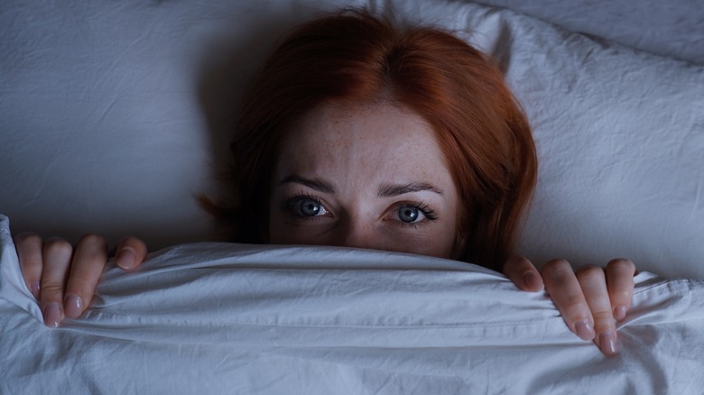afraid woman hiding under duvet in bed
