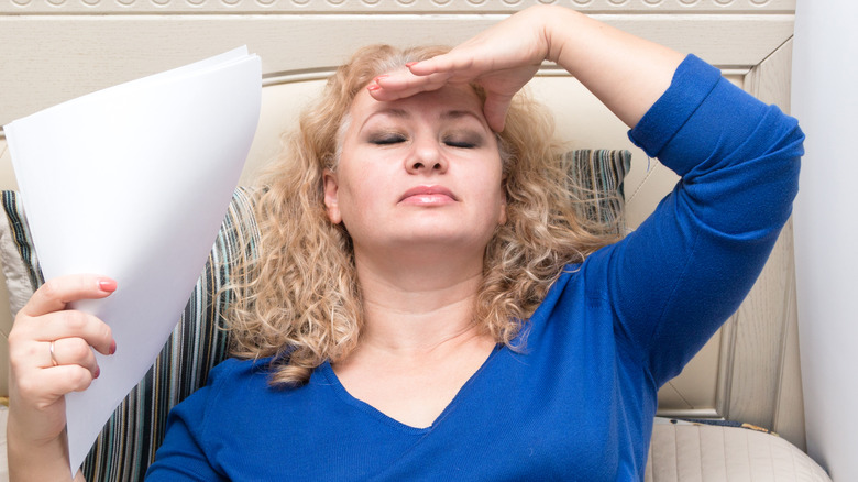 Woman in bed with hot flash fanning herself with piece of paper