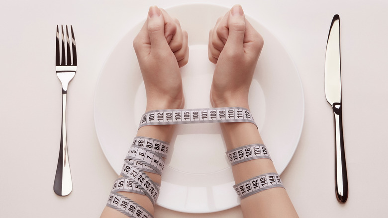Woman having her hands tied with a meter scale over an empty plate