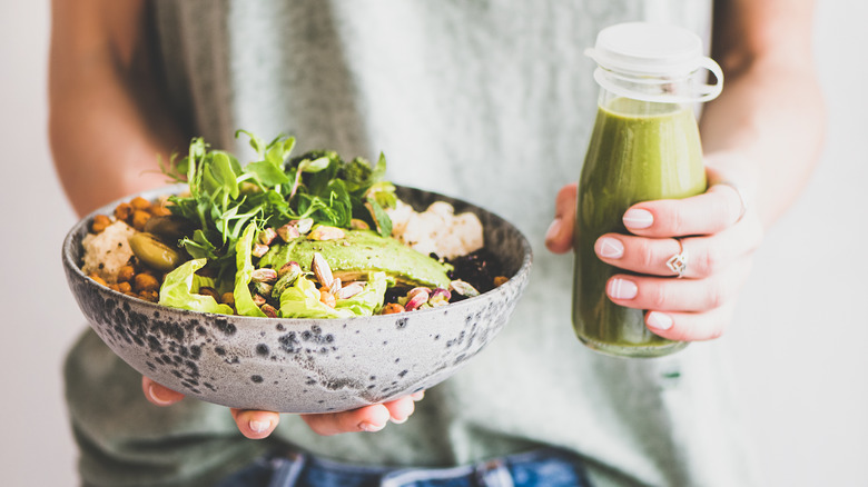 Person holding green smoothie and veggie bowl