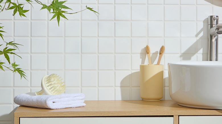 Toothbrushes stored in a cup beside a ceramic sink.