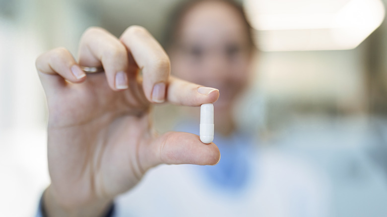 women in background holding capsule pill for photo