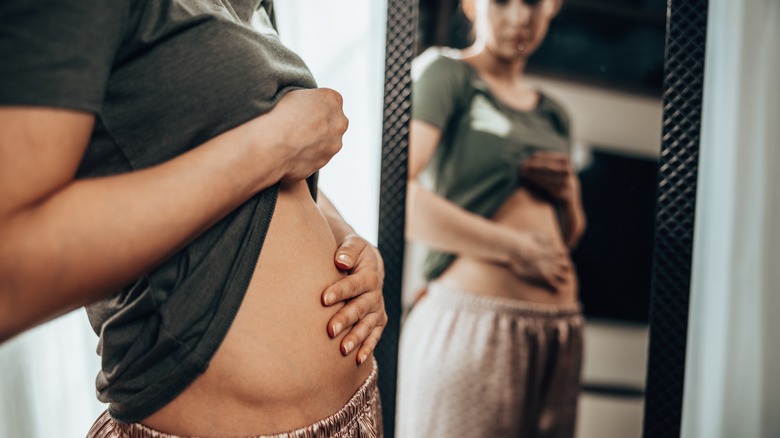 Woman touching her stomach and looking in mirror