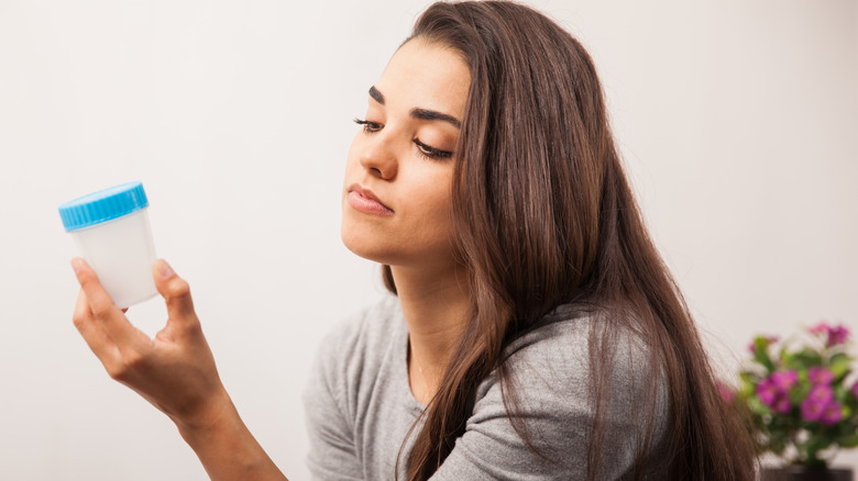 Woman holding urine sample collection cup