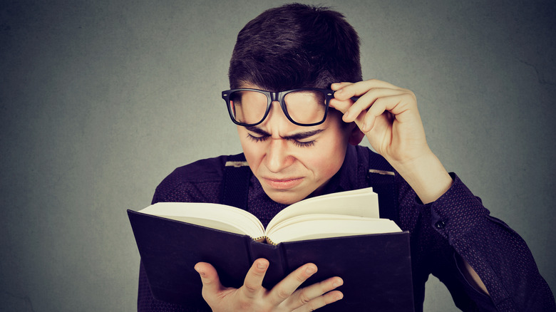 Man raises his glasses and squints to read a book