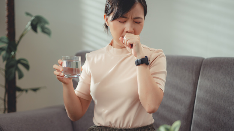 woman coughing holding glass of water