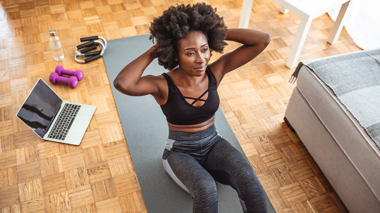 Woman dressed in black sports bra and grey leggings doing sit up on yoga mat