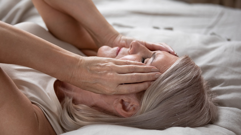 Woman with migraine laying on bed holding temples