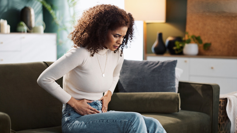 A woman sitting on her couch with lower abdominal pain