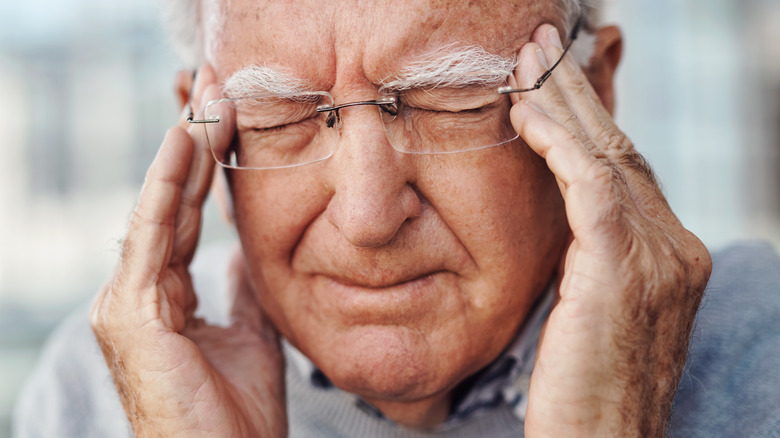 Elderly bespectacled man rubbing eyebrows