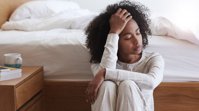 woman with a migraine sitting by her bed