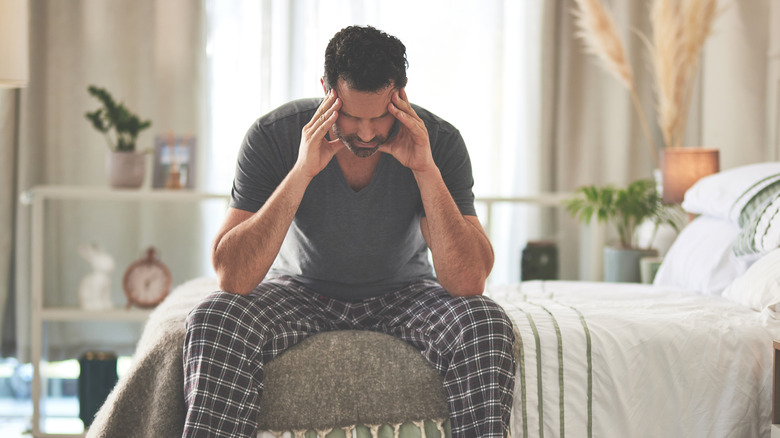 man sitting at the edge of his bed with a headache