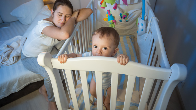 Woman sleeping next to baby awake in crib
