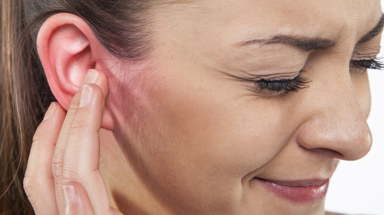 Wincing woman touching red ear