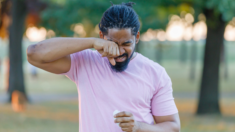 man outdoors rubbing his sore eyes