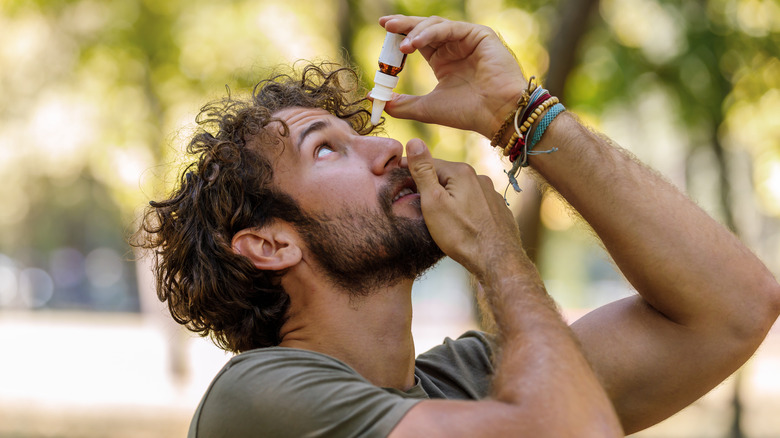 man outside putting eye drops into his eye