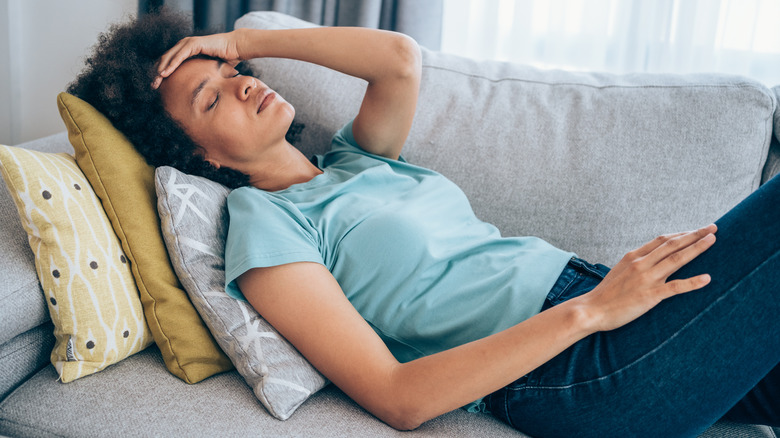 woman holding head lying on couch