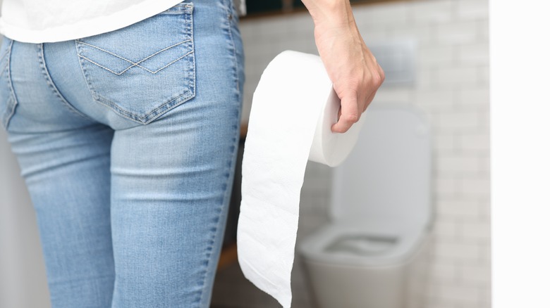 Person in bathroom holding toilet paper