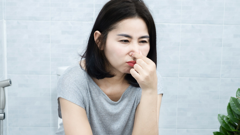 Woman holding nose in bathroom