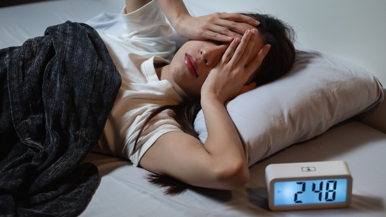 Person laying in bed covering their eyes trying to sleep next to an alarm clock that reads "2:48"