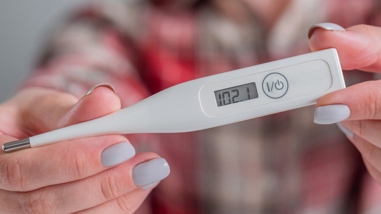 Woman holding thermometer with high temperature