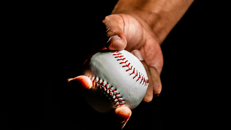 A hand holding a baseball against a dark backdrop
