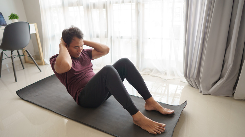 Man on yoga mat at home doing a sit-up