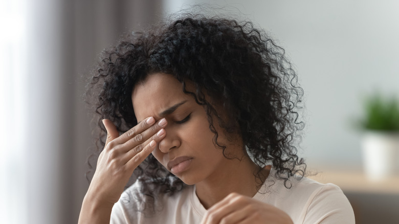 Woman grimacing with closed eyes and hand on face